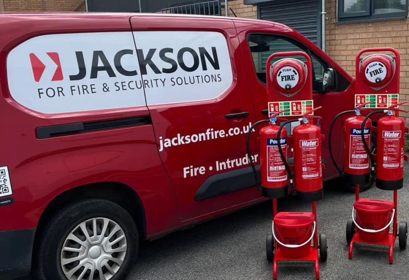 Jackson Fire & Security branded van parked alongside red Powder and Water fire extinguishers on commissioning trolleys, ready for site delivery and servicing